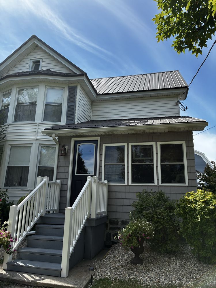 Gray two-story house with white trim, front steps, and a small porch under a sunny blue sky