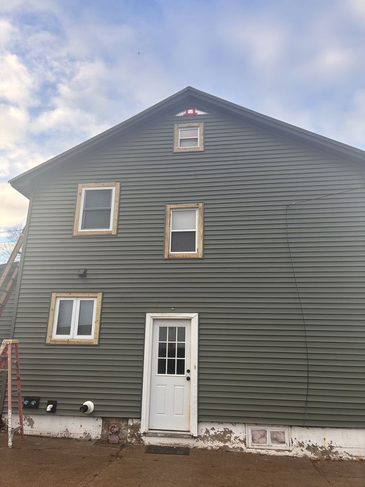 Gray-sided house exterior with white trim, a front door, and windows under a cloudy sky