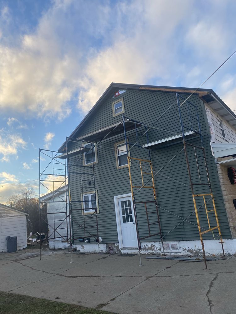 Two-story house with scaffolding and a ladder on the front under a partly cloudy sky