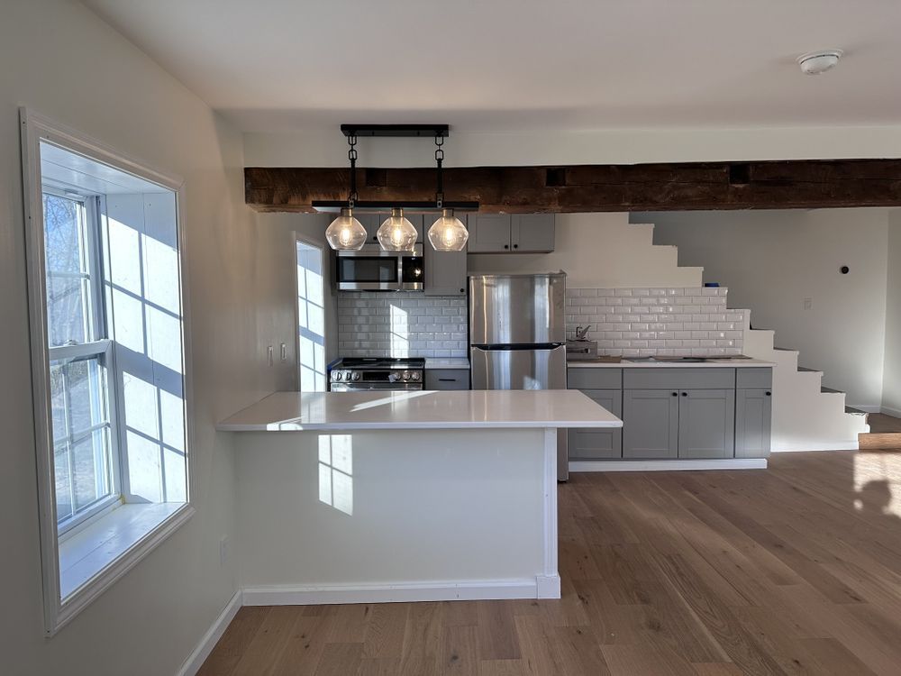 Bright modern kitchen and dining area with white island, stainless fridge, pendant lights, and wood floors
