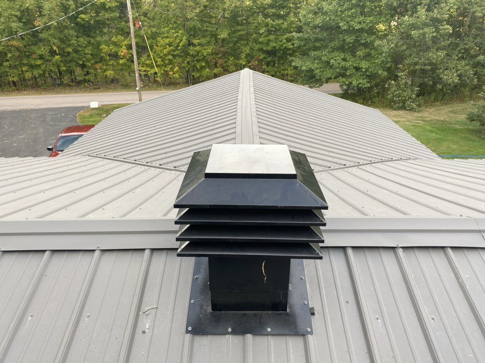 Black rooftop vent on gray metal roof with trees in the background