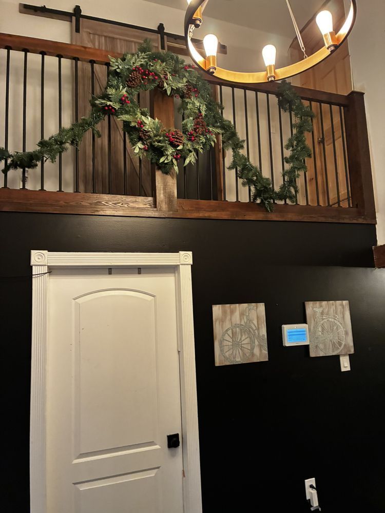 Interior entryway with a white door, black wall, wooden railing, and holiday garland on the upstairs balcony.