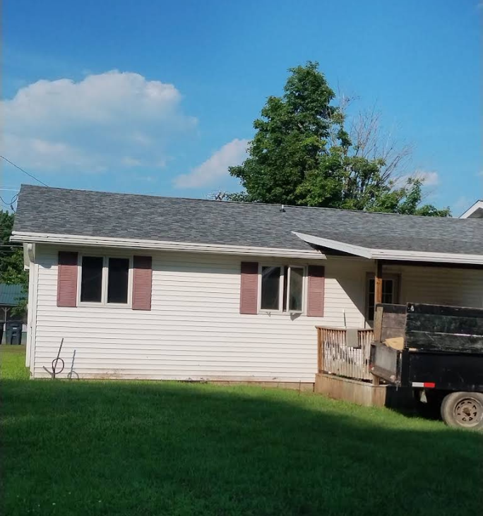 Single-story beige house with red shutters, green lawn, blue sky, and a truck parked beside the porch