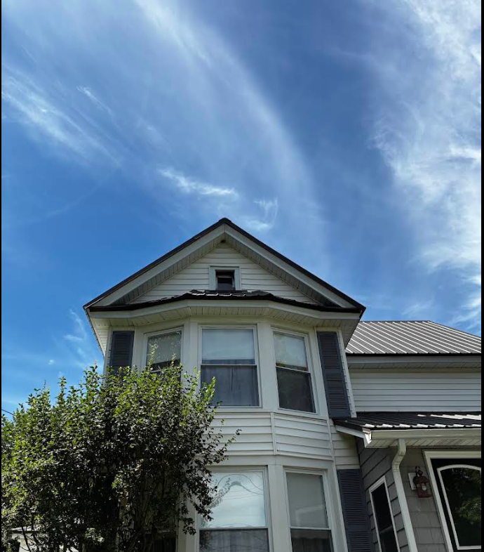 Victorian-style house with a bay window and white siding under a bright blue sky