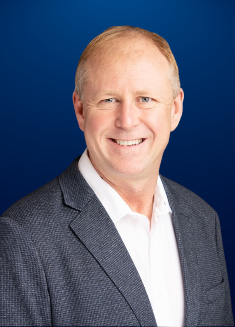 A man in a suit and white shirt is smiling in front of a blue background.