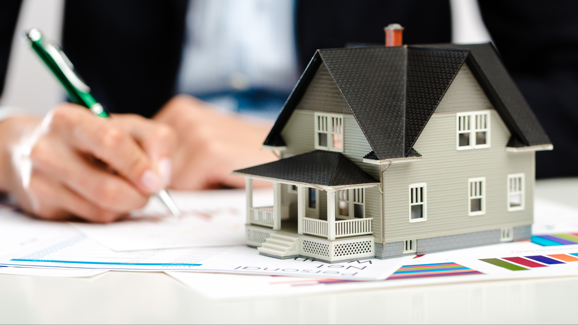 A person is writing on a piece of paper next to a model house.
