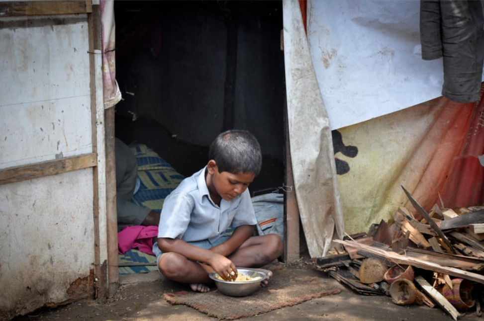 A young boy is sitting on the ground eating food from a bowl.