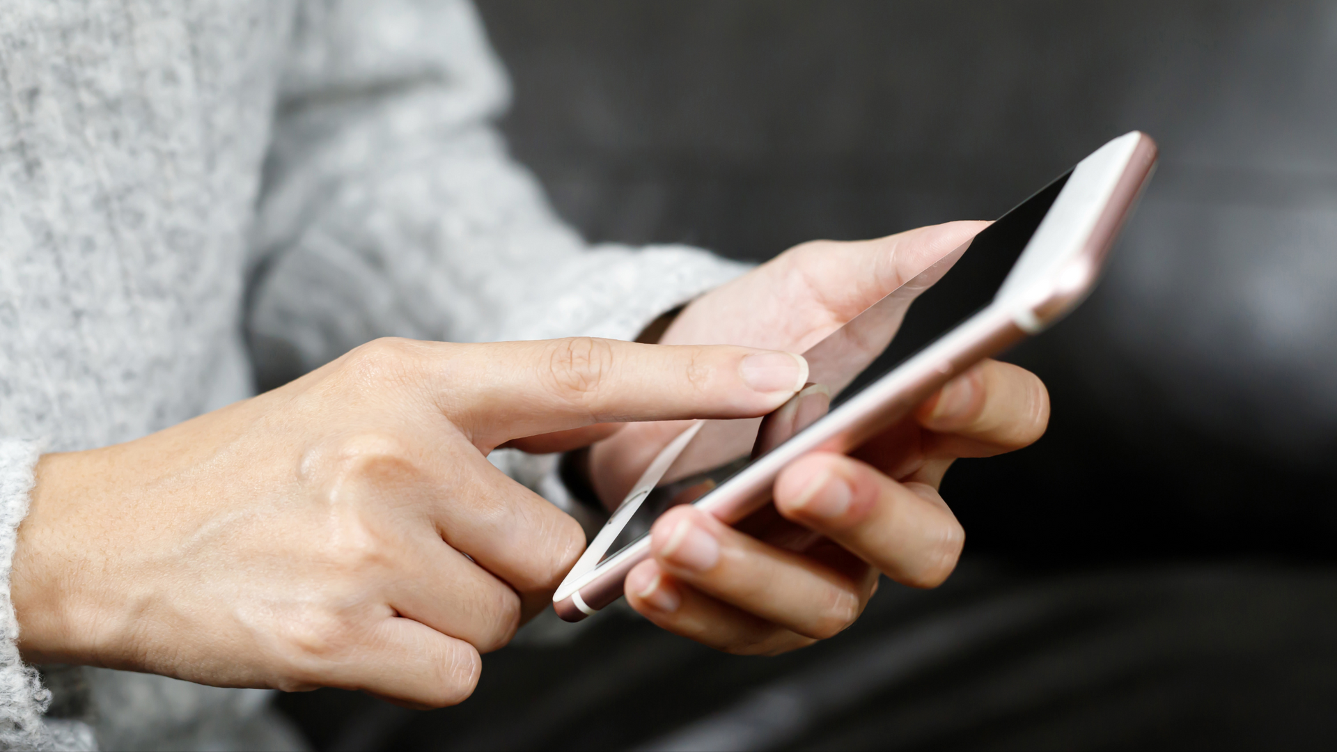 A woman is using a cell phone while sitting on a couch.