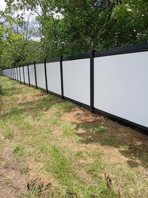 A white and black fence surrounds a grassy field.