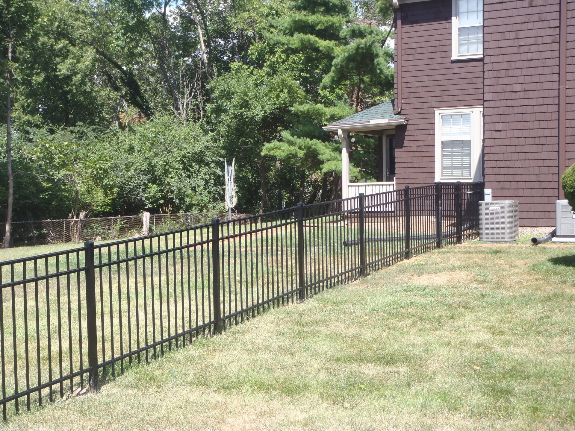A long black metal fence surrounds a grassy area. A long black metal fence surrounds a grassy area.