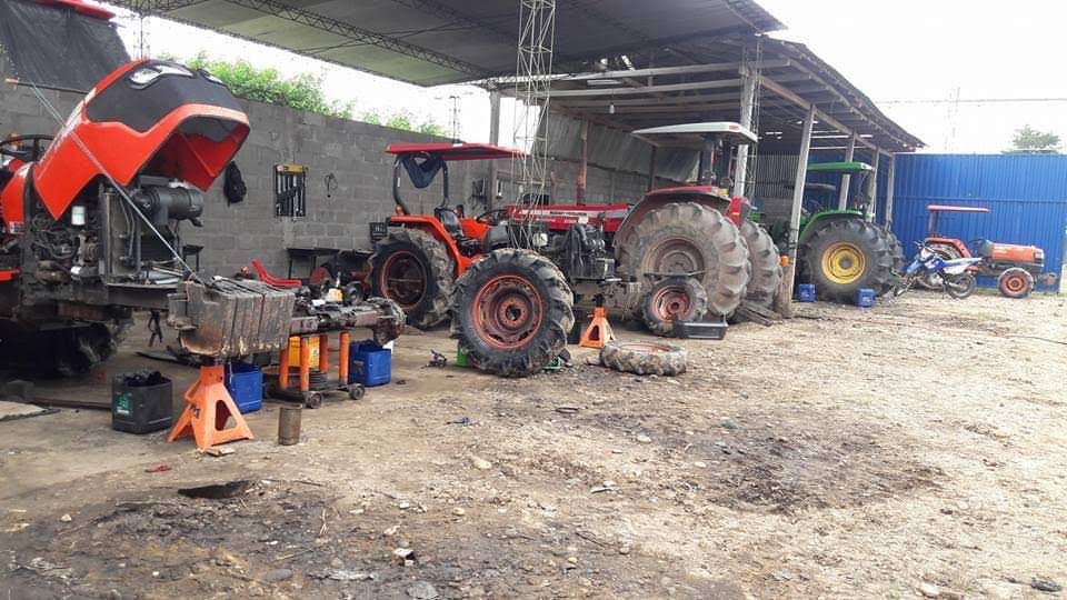 Tractores en un taller de reparación con capós levantados y herramientas esparcidas en el suelo.