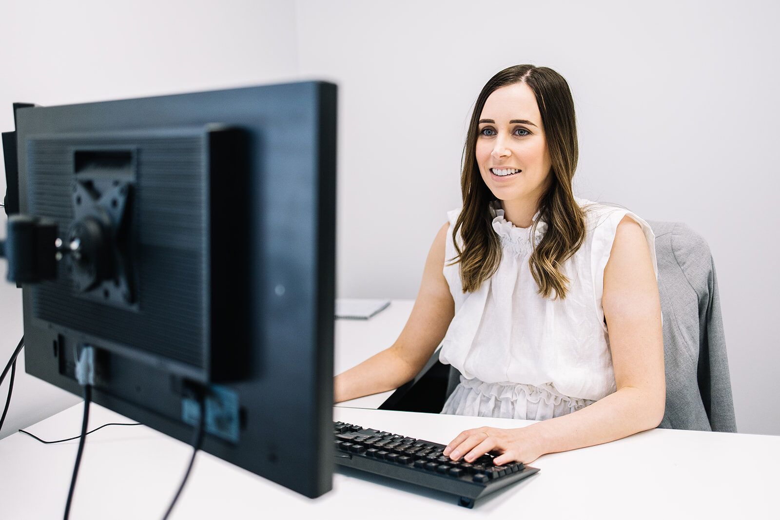 A Woman Is Sitting At A Desk In Front Of A Computer Monitor — The Garis Group  In Hamilton, NSW