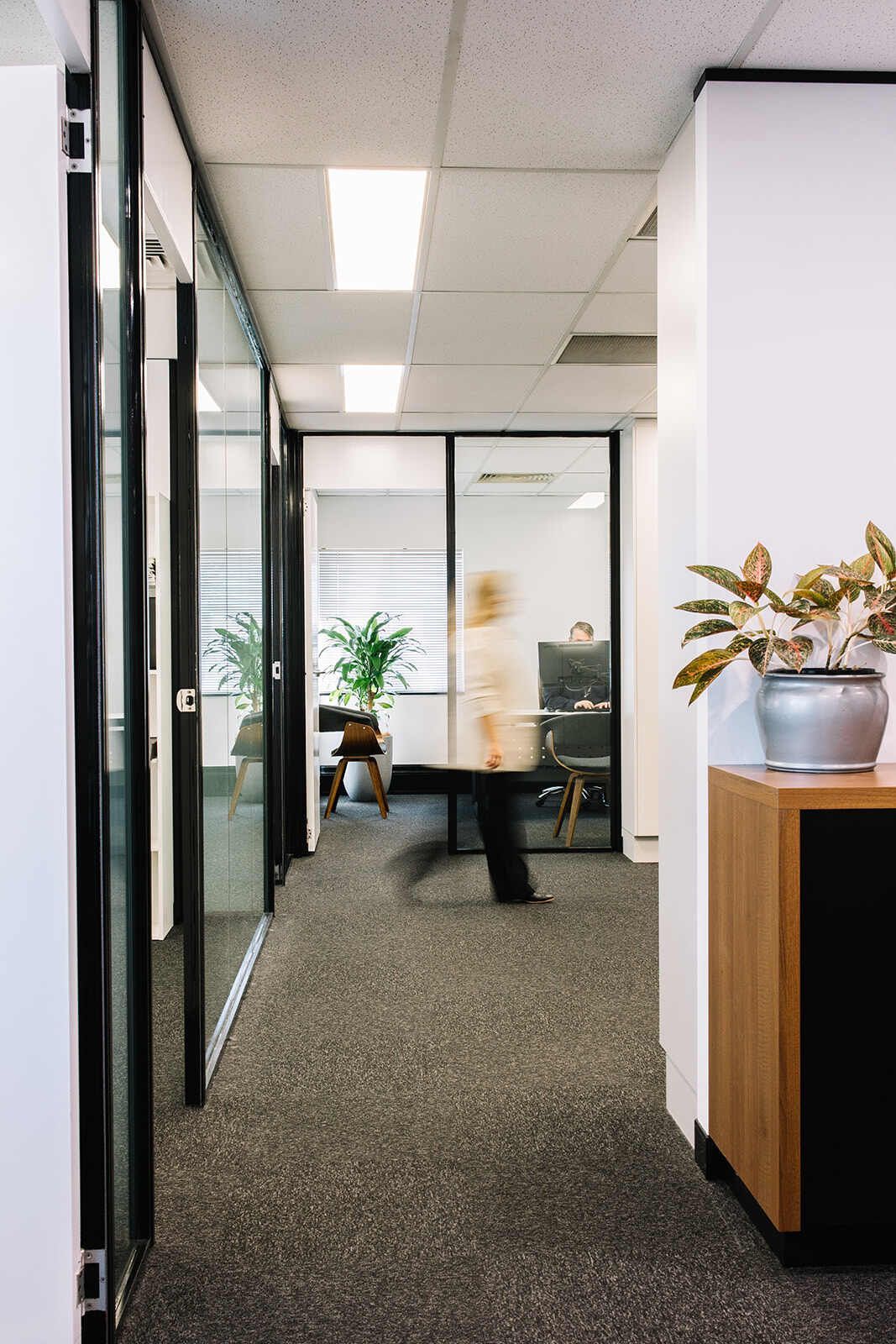 A Woman Is Walking Down A Hallway In An Office Building — The Garis Group In Hamilton, NSW