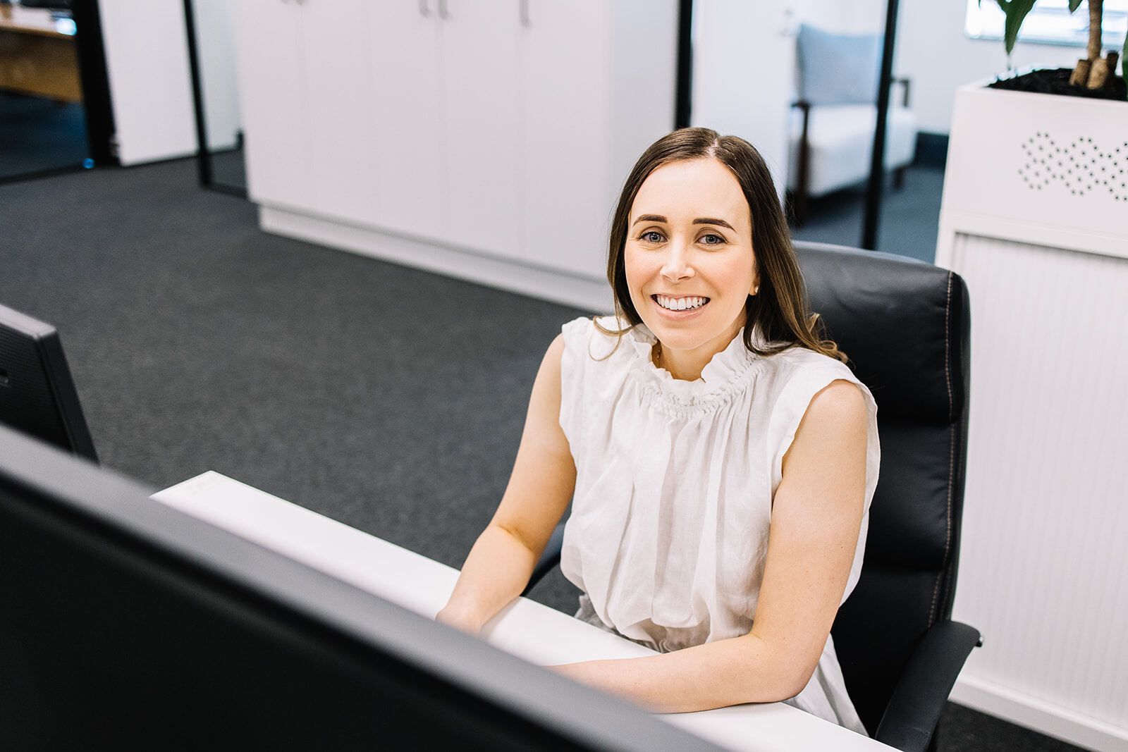 A Woman Is Sitting At A Desk In Front Of A Computer And Smiling — The Garis Group  In Hamilton, NSW 