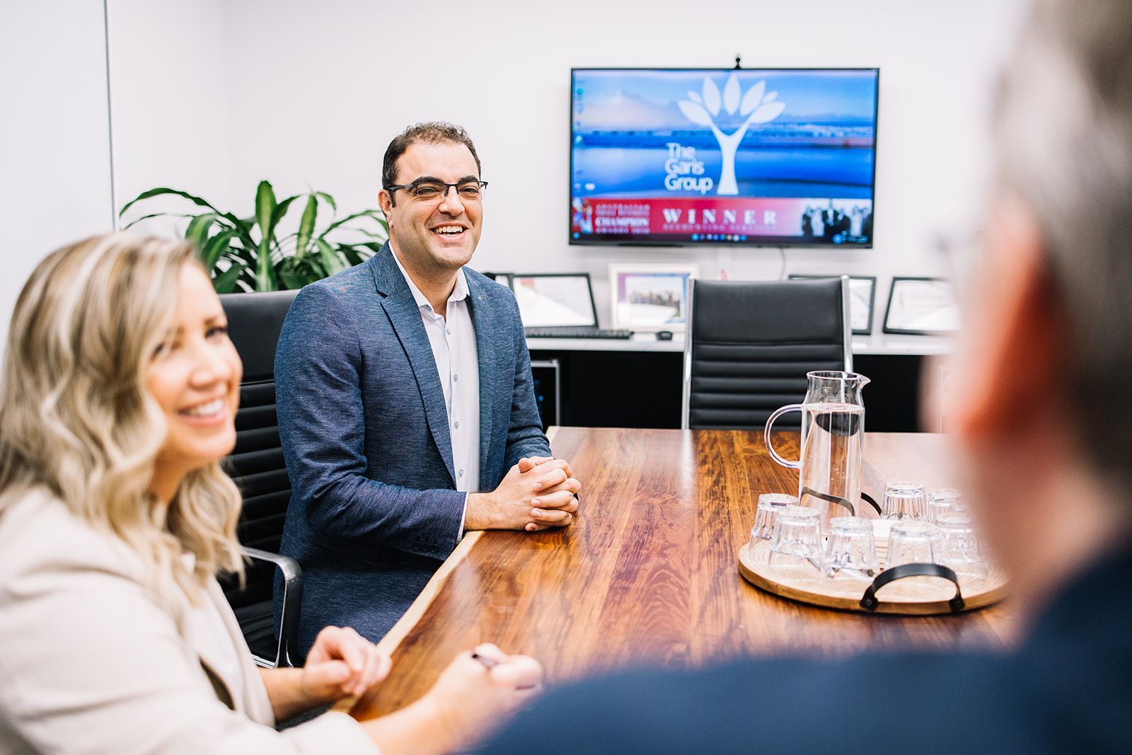 A Woman Is Sitting At A Desk In Front Of A Computer And Smiling — The Garis Group In Hamilton, NSW