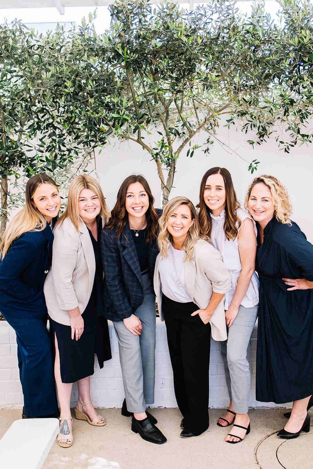 A Group Of Women Are Posing For A Picture In Front Of A Tree — The Garis Group In Hamilton, NSW