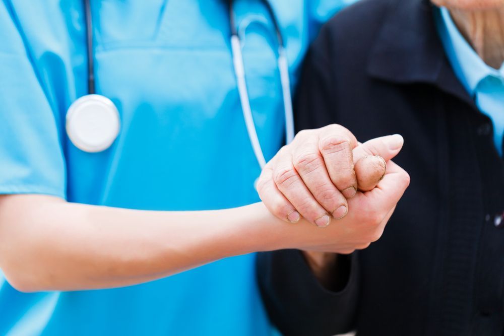 A Nurse Is Holding The Hand Of An Elderly Woman — The Garis Group  In Hamilton, NSW 