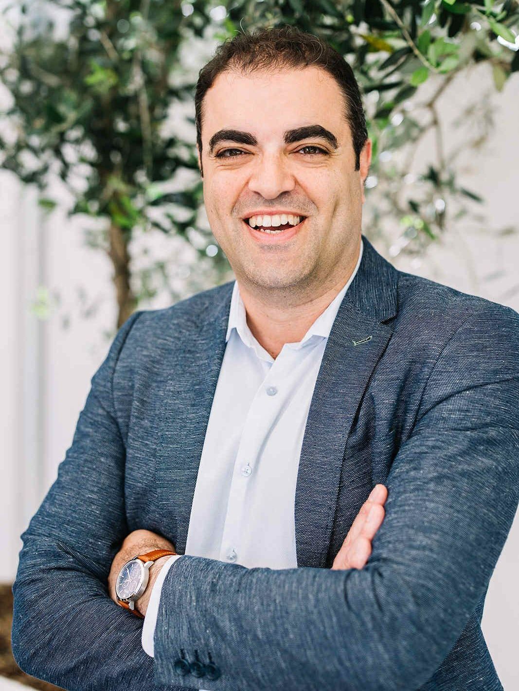 A Man in a Suit and White Shirt is Smiling With His Arms Crossed — The Garis Group  In Hamilton, NSW 