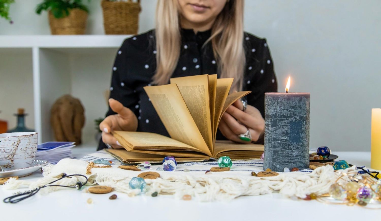 Person at a table arranging a gold folding paper craft beside a lit candle and crystals