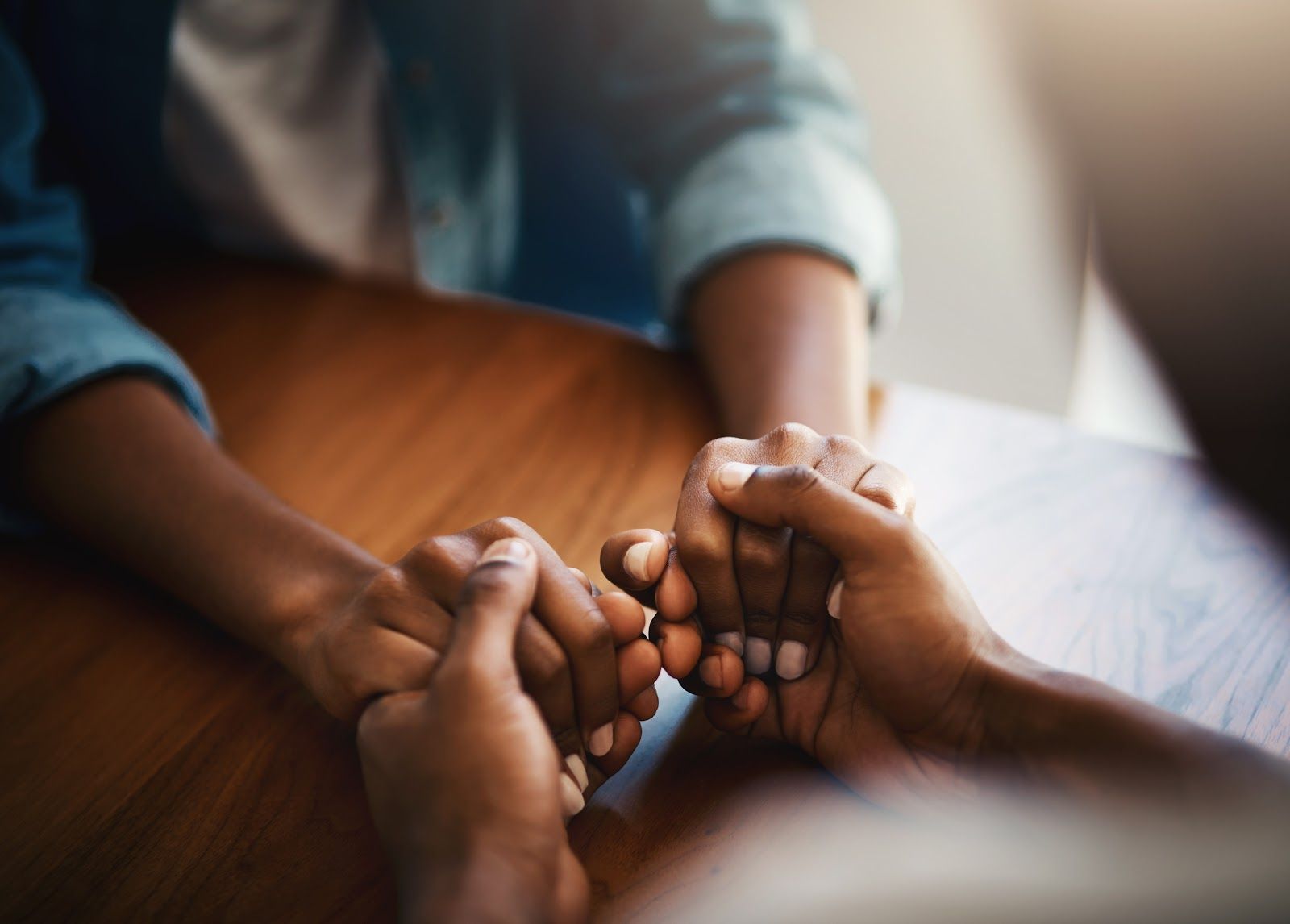 Hands clasped together in a supportive gesture over a wooden table