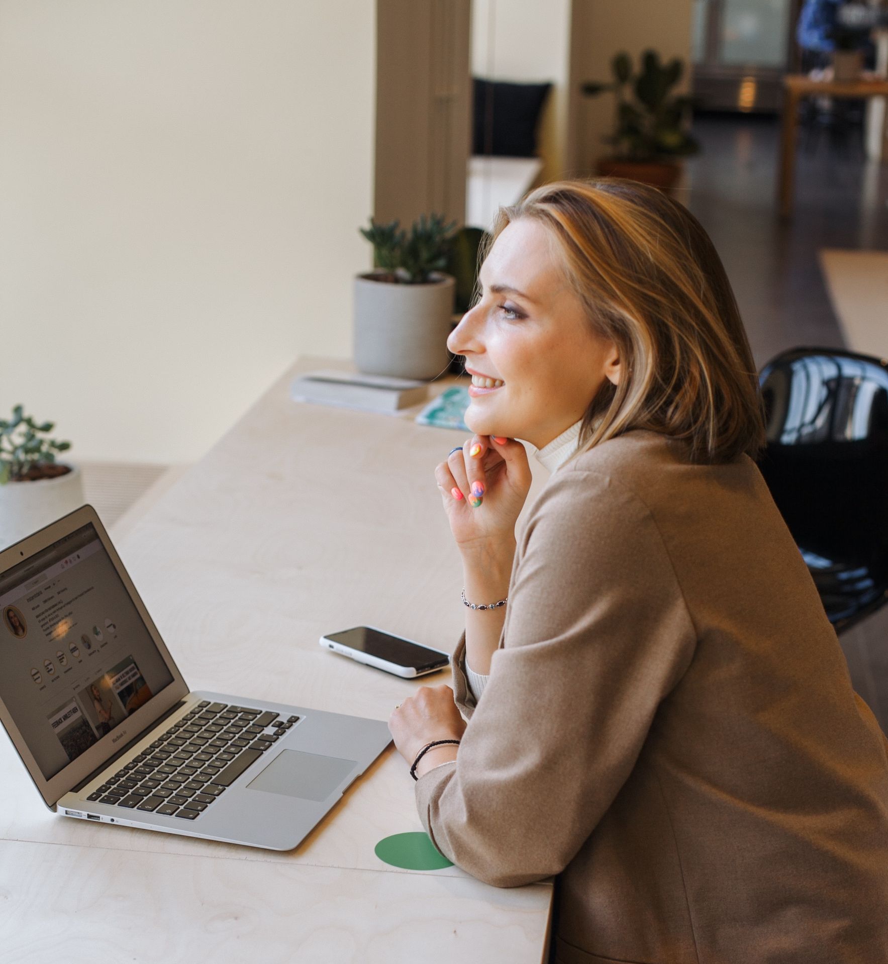 a professional woman sits at a desk looking at a laptop