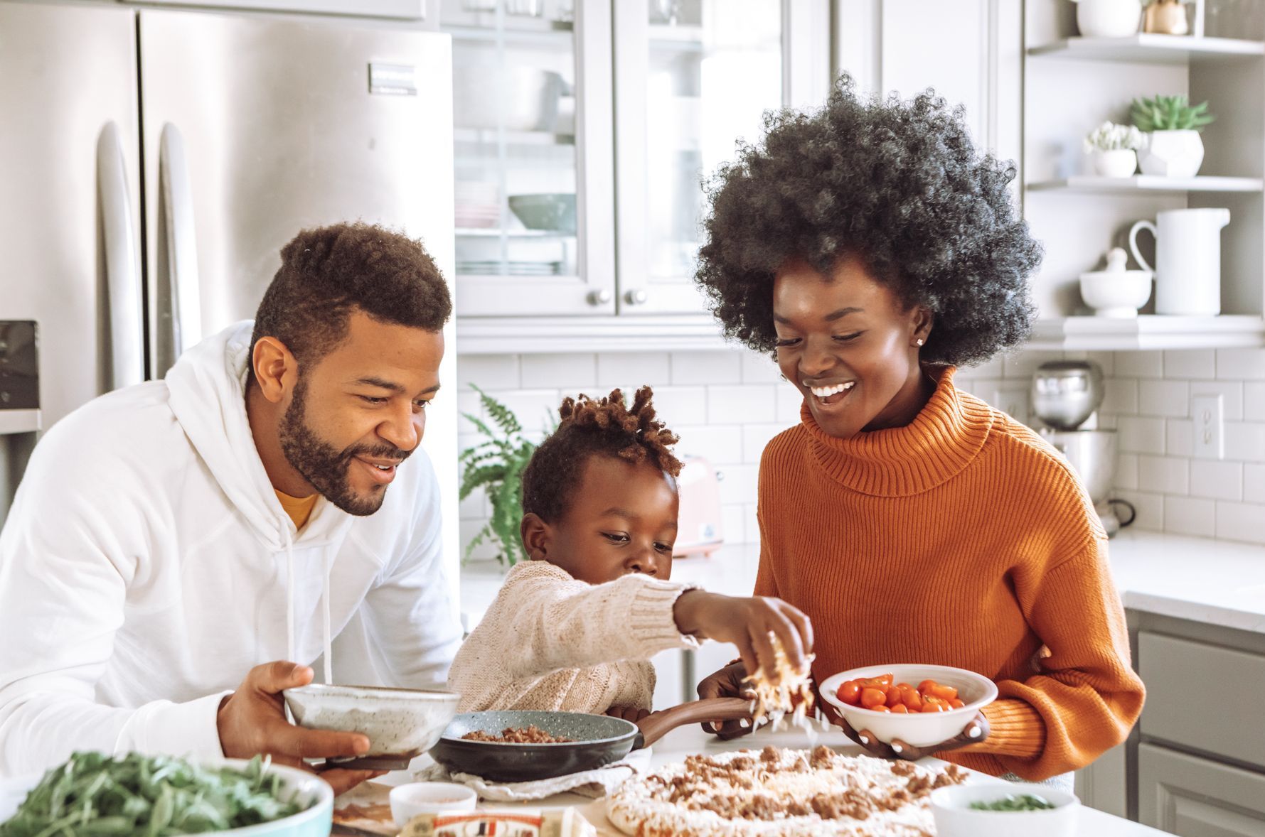 a family prepares food in a kitchen with a refrigerator in the background