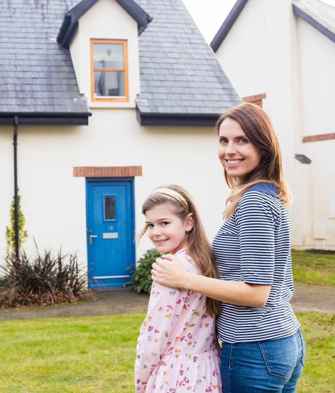 a woman and a little girl are standing in front of a white house with a blue door