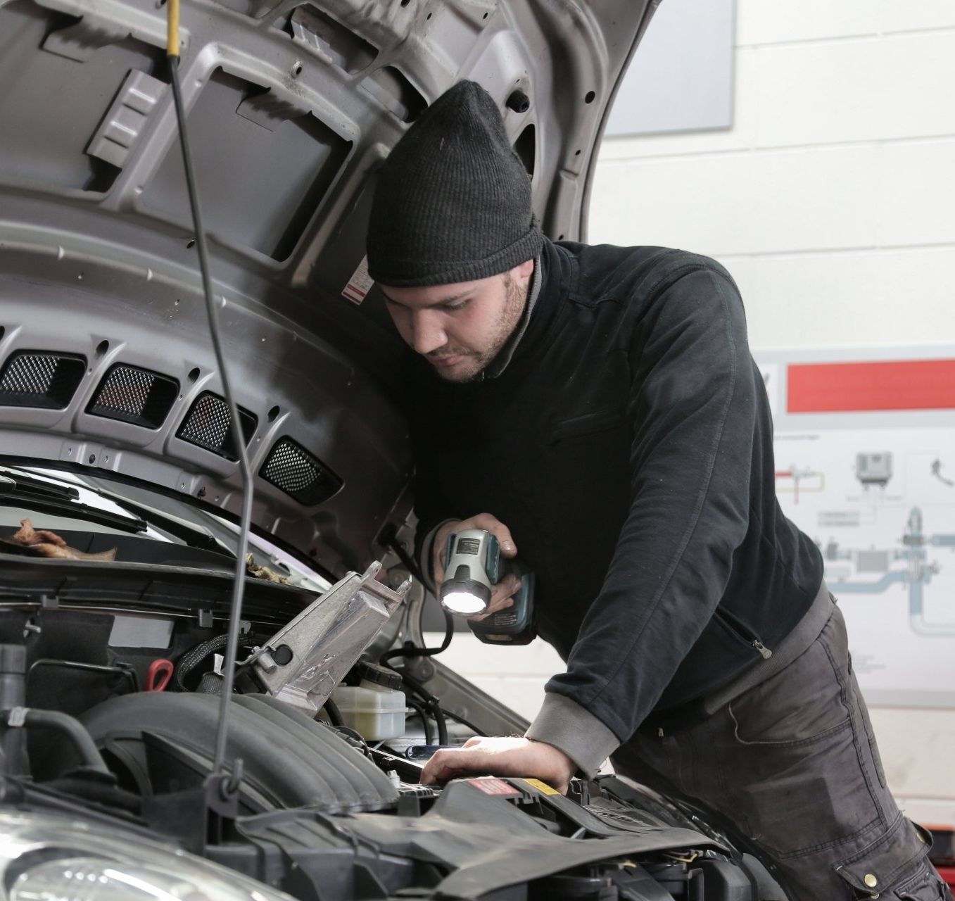 a man looking under the hood of a car with a flashlight