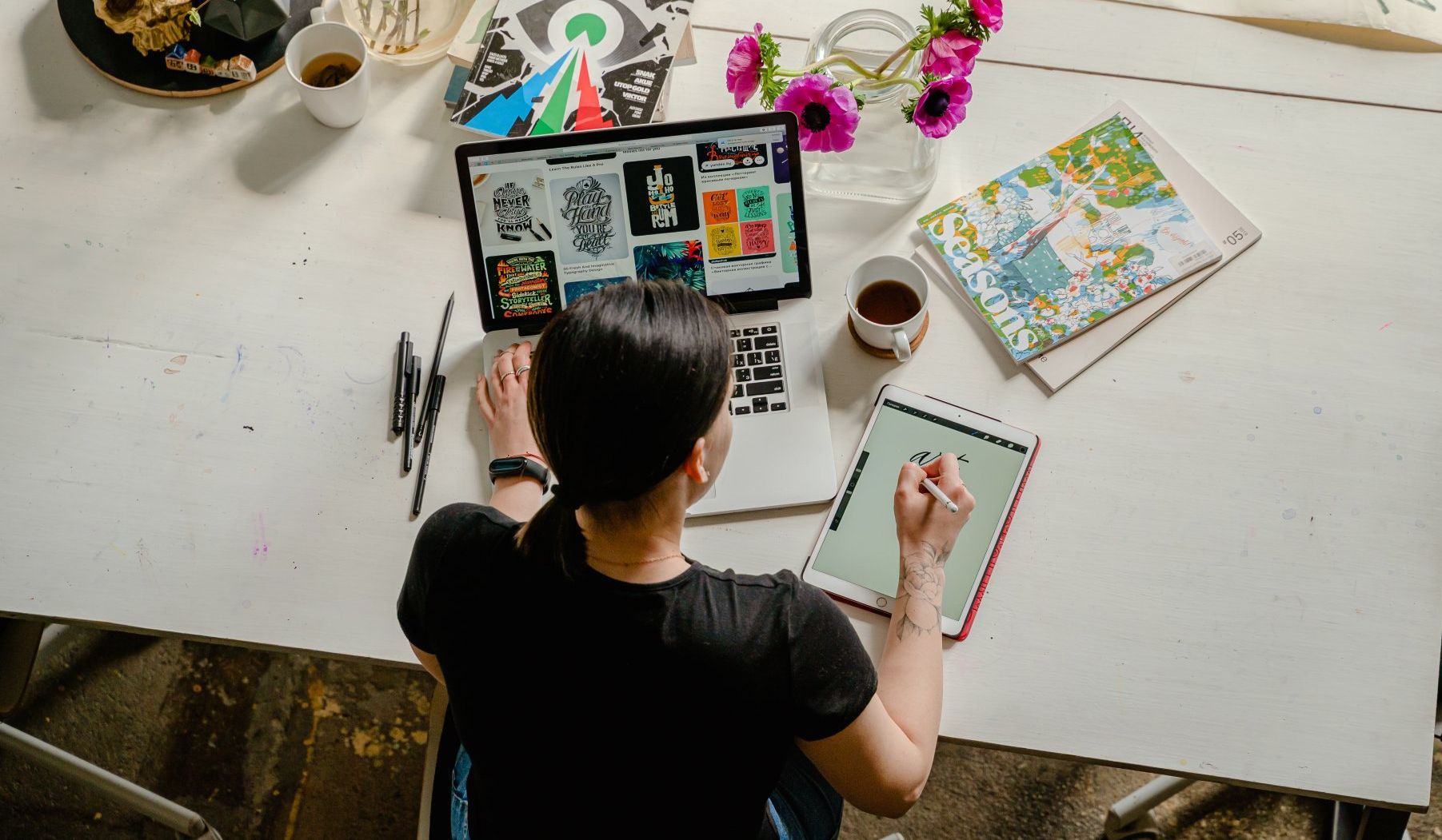 a woman sits at a desk using a laptop and a tablet