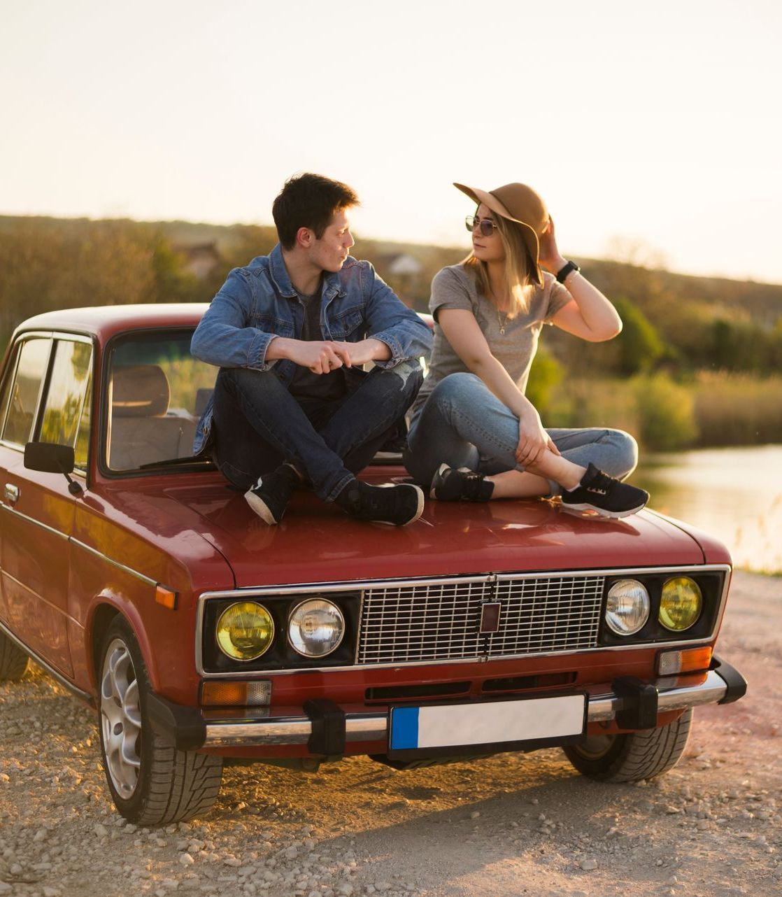 a man and a woman sit on the hood of a red car