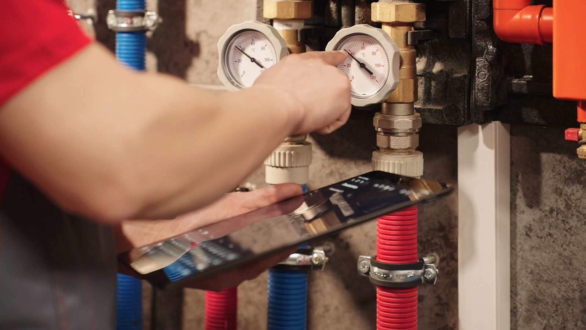 Technician adjusting pressure gauges on industrial pipes and valves in a mechanical room