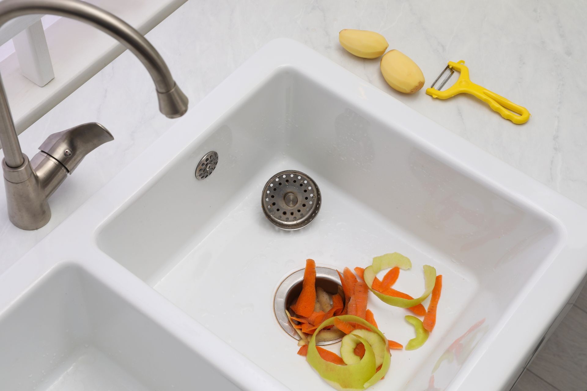 Kitchen sink with peeled vegetable scraps and a yellow peeler on the counter