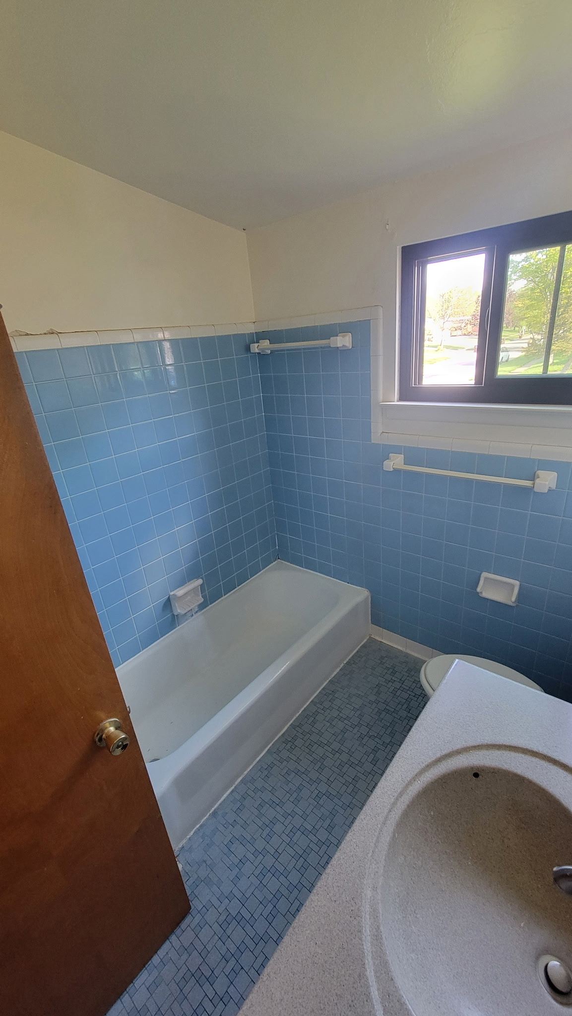 Blue-tiled bathroom with a bathtub, sink, and small window.