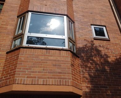 Fachada de un edificio de apartamentos de ladrillo con un ventanal y la luz del sol reflejándose en el cristal.