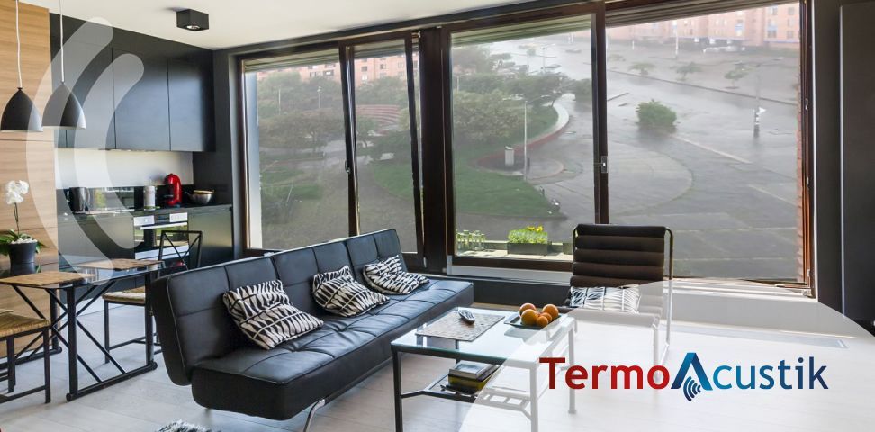 Sala de estar moderna con sofá negro, mesa de centro de cristal y grandes ventanales con vistas a una calle.