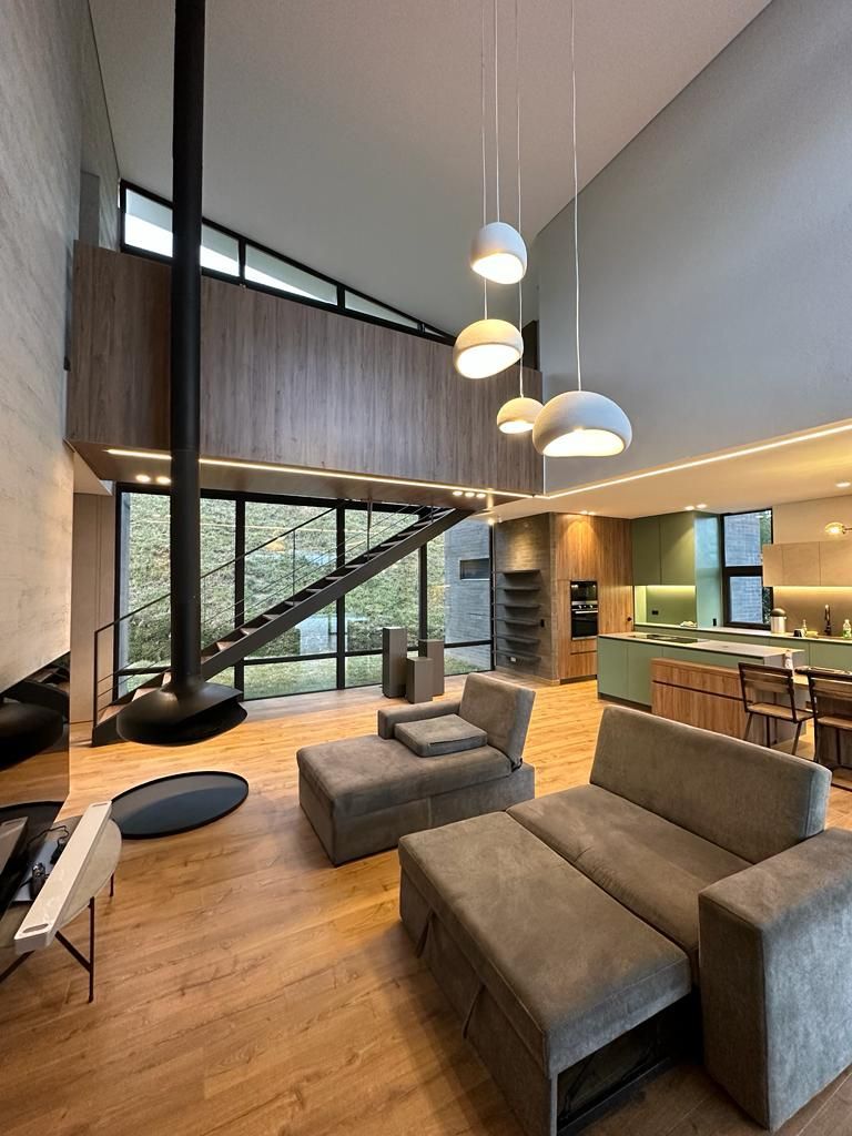 Sala de estar moderna con sofá modular, lámparas colgantes, suelos de madera y una gran ventana en la escalera.