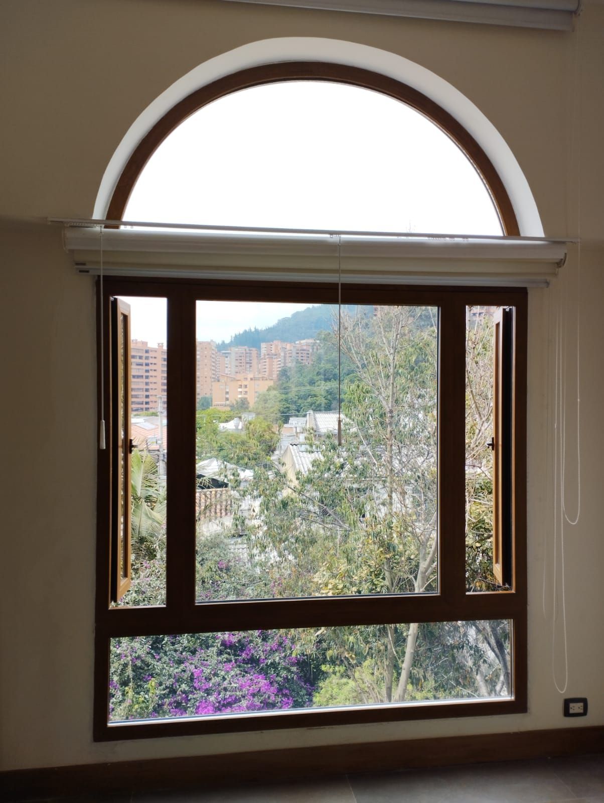 Ventana con arco superior con vistas a árboles, flores y colinas lejanas a la luz del día.