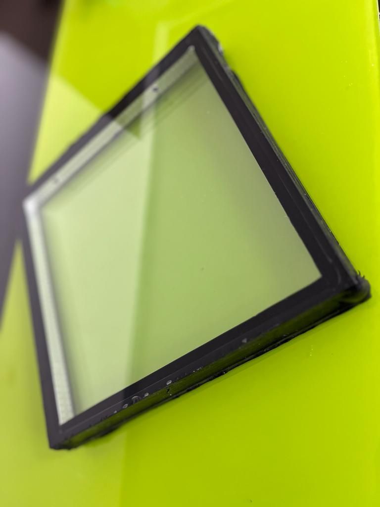 Panel de vidrio con marco negro que descansa sobre una superficie de color amarillo brillante.