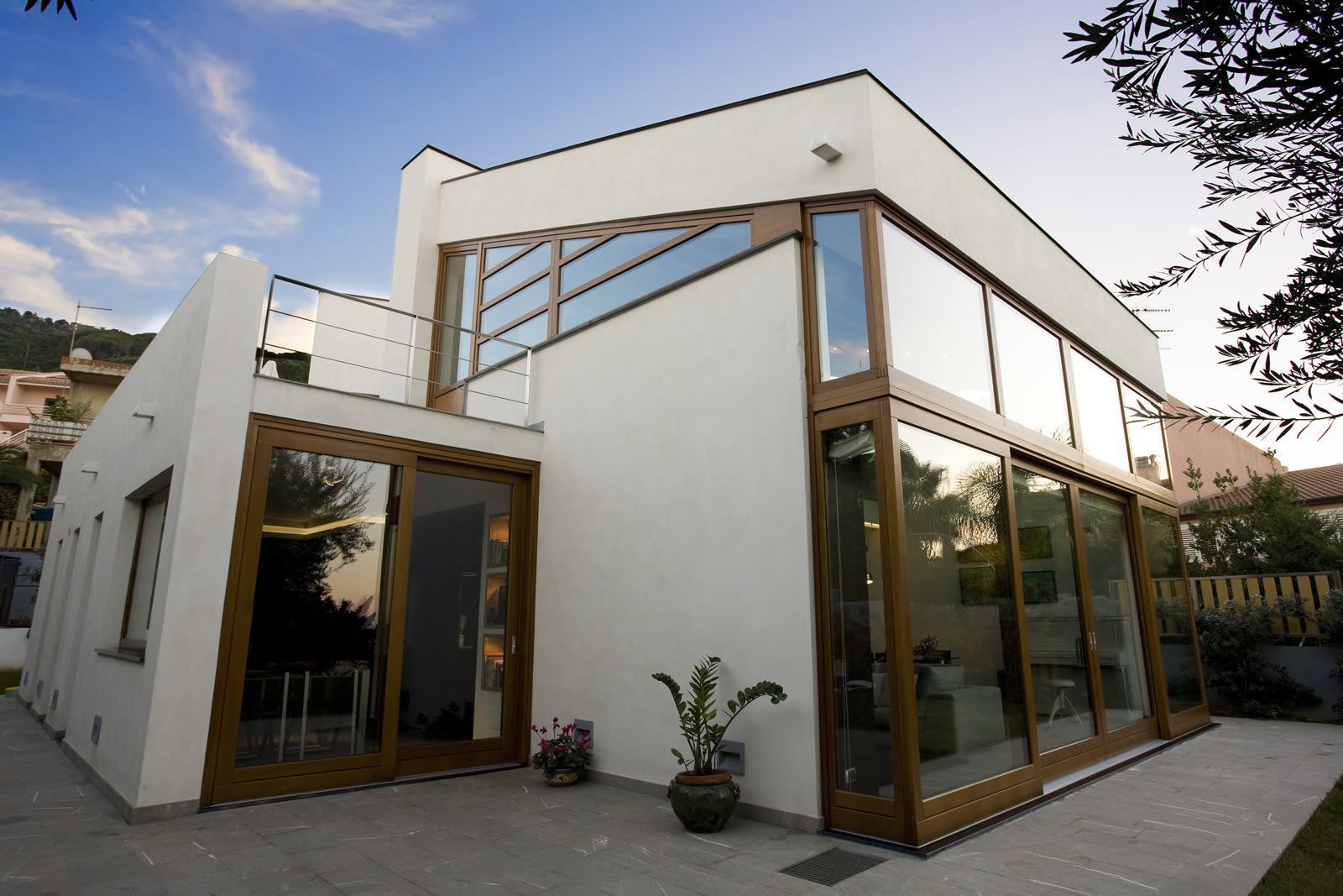Casa moderna de color blanco con grandes ventanales y detalles de madera, vista desde el patio.