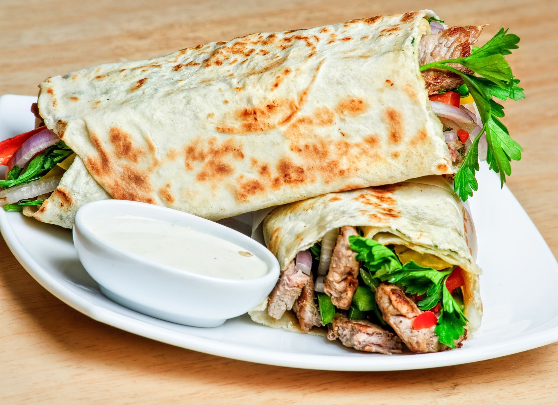 A white plate topped with a wrap and a dipping sauce.