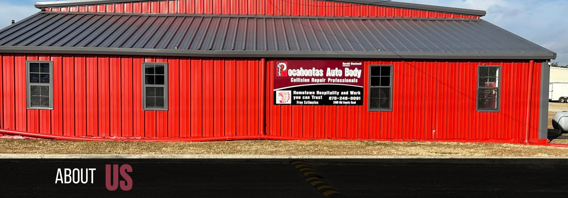 Red building with a gray roof, black windows, and a sign reading “About Us” near the bottom.