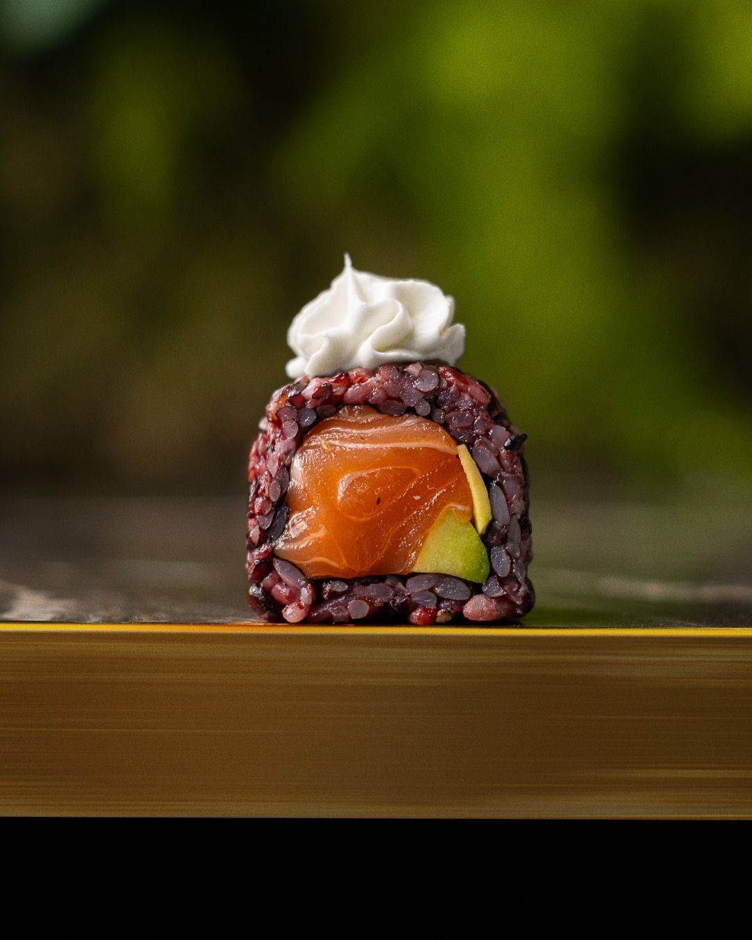 Rotolo di sushi con salmone, avocado e panna montata, su una superficie dorata.