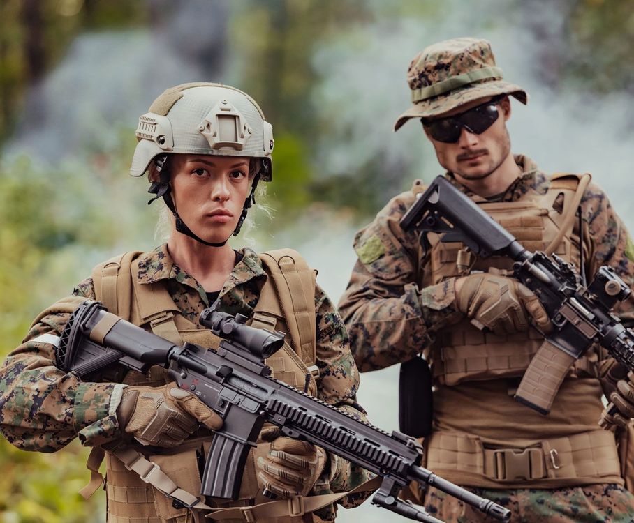 Two soldiers in camouflage uniforms and tactical gear stand in a smoky outdoor environment, holding assault rifles.