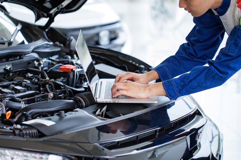 A Man is Working on the Engine of a Car While Using a Laptop — Hive Mobile Roadworthy in Mount Nathan, QLD