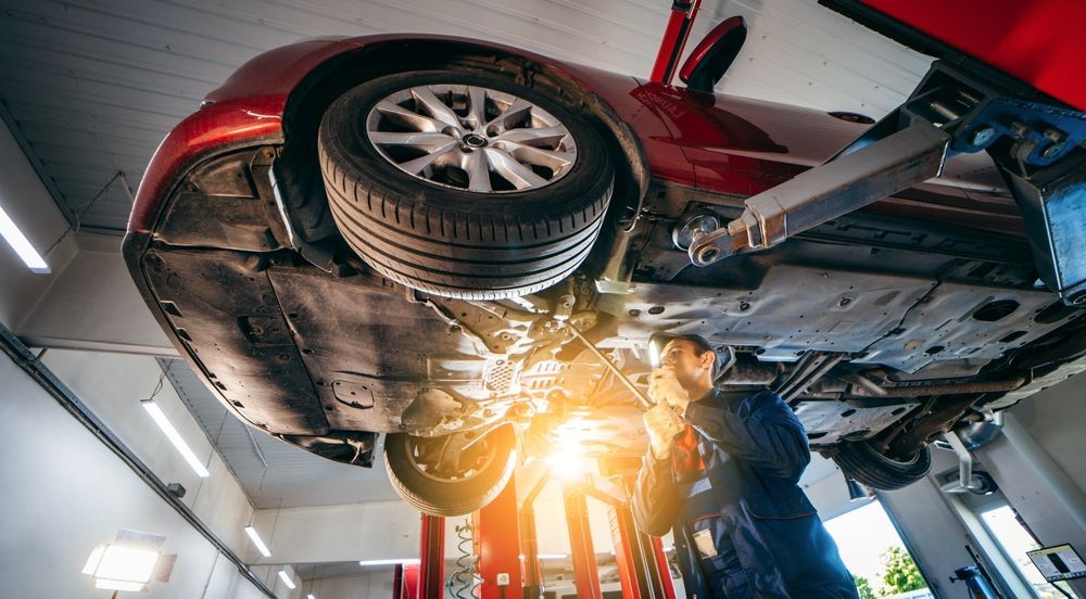 Two Mechanics Inspecting a Red Car Lifted on a Repair Hoist — Hive Mobile Roadworthy in Palm Beach, QLD