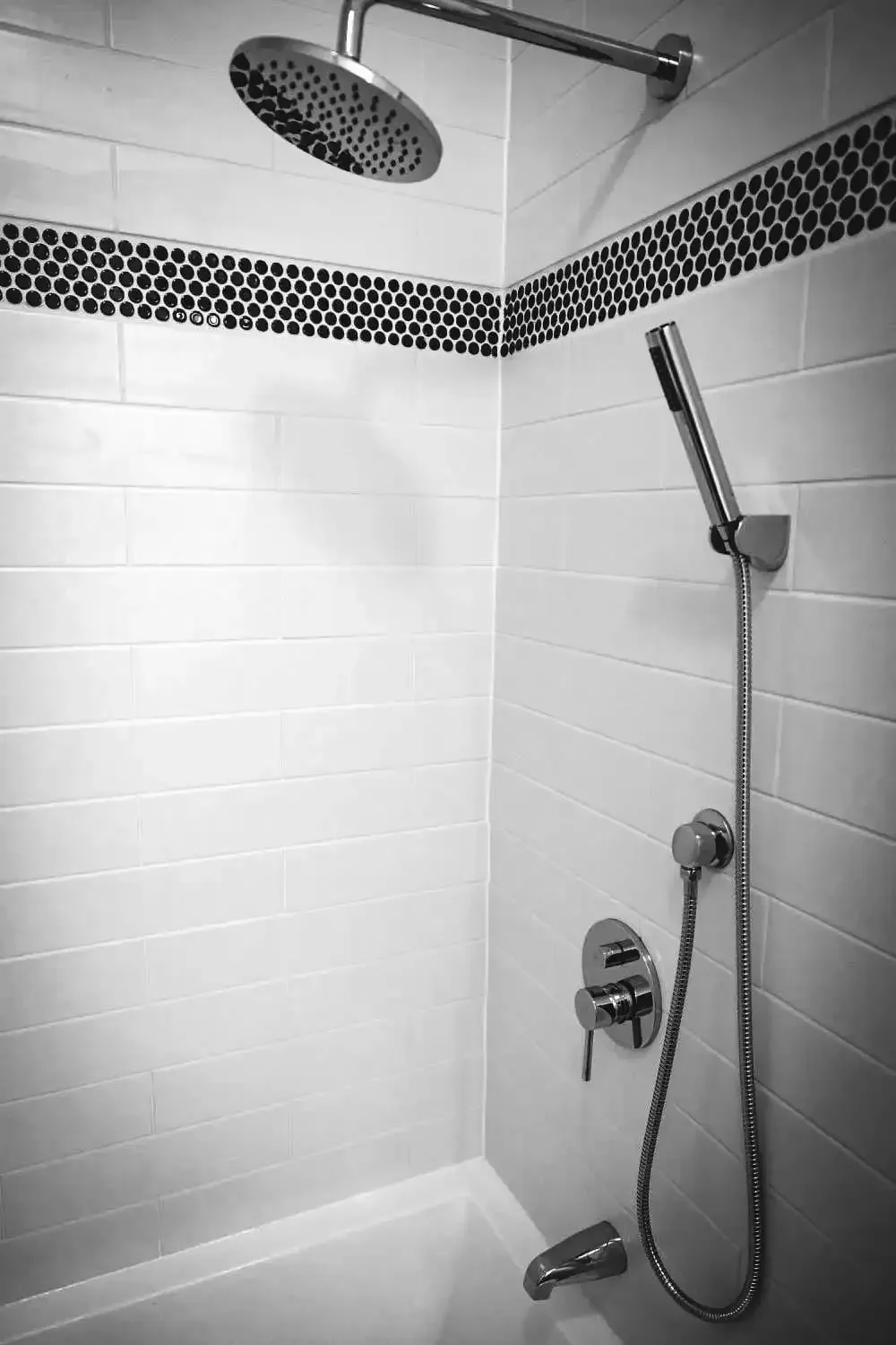 A black and white photo of a shower with a shower head and hose.