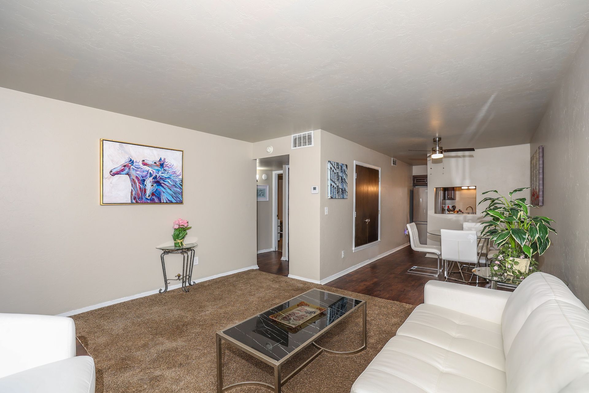 Living room with white couch, rug, art, and dining area in the background.