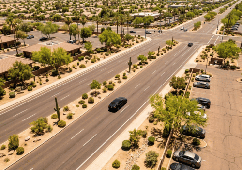 Aerial view of a desert city boulevard with landscaped medians, scattered cacti, and light traffic.