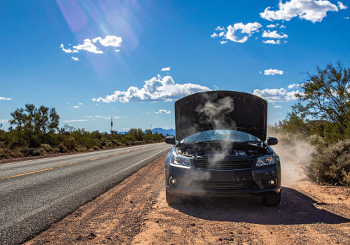 Car stopped on a roadside with the hood open and steam rising from the engine.