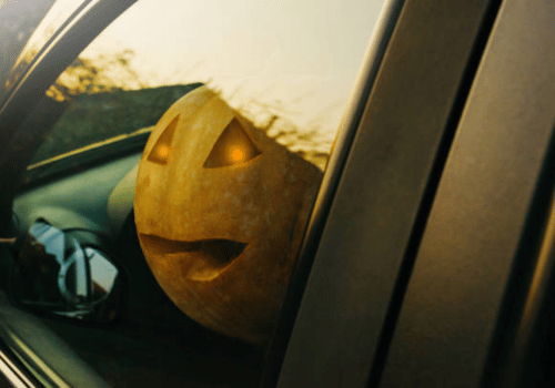 Glowing jack-o'-lantern in a car window at sunset